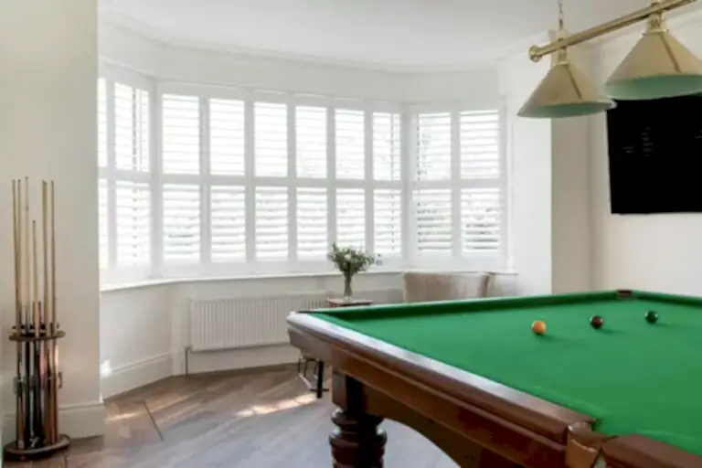 plantation shutters in large bay window with pool table Plantation Shutters Project - Your #1 Choice for Shutters NI